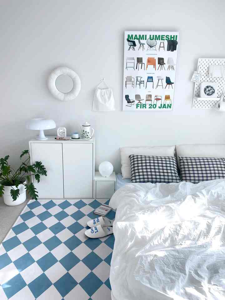Pastel white and blue bedroom featuring checkered rug and clean furniture, presenting a simple and modern atmosphere