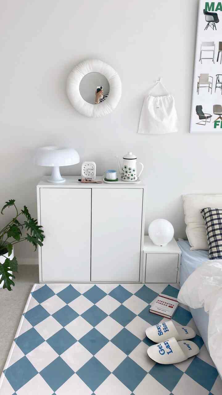 明るい白と青のトーンのワンルームリビング、チェッカーパターンのラグとシンプルな収納家具がミニマルなインテリアを演出