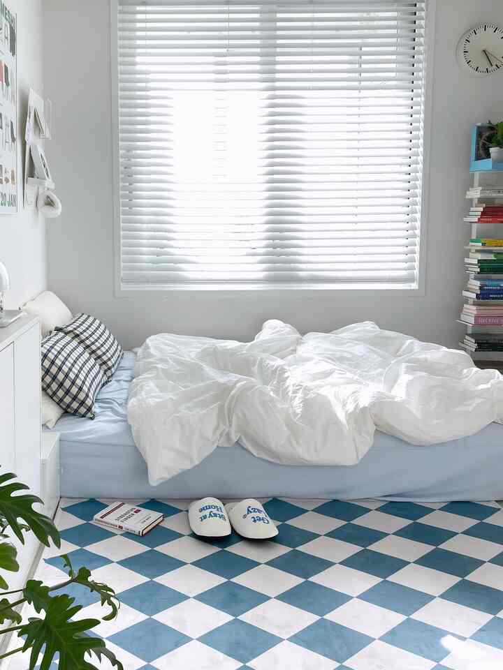 Bright white and blue bedroom with a central bed featuring white bedding, a bookshelf on the right, styled simply with natural light