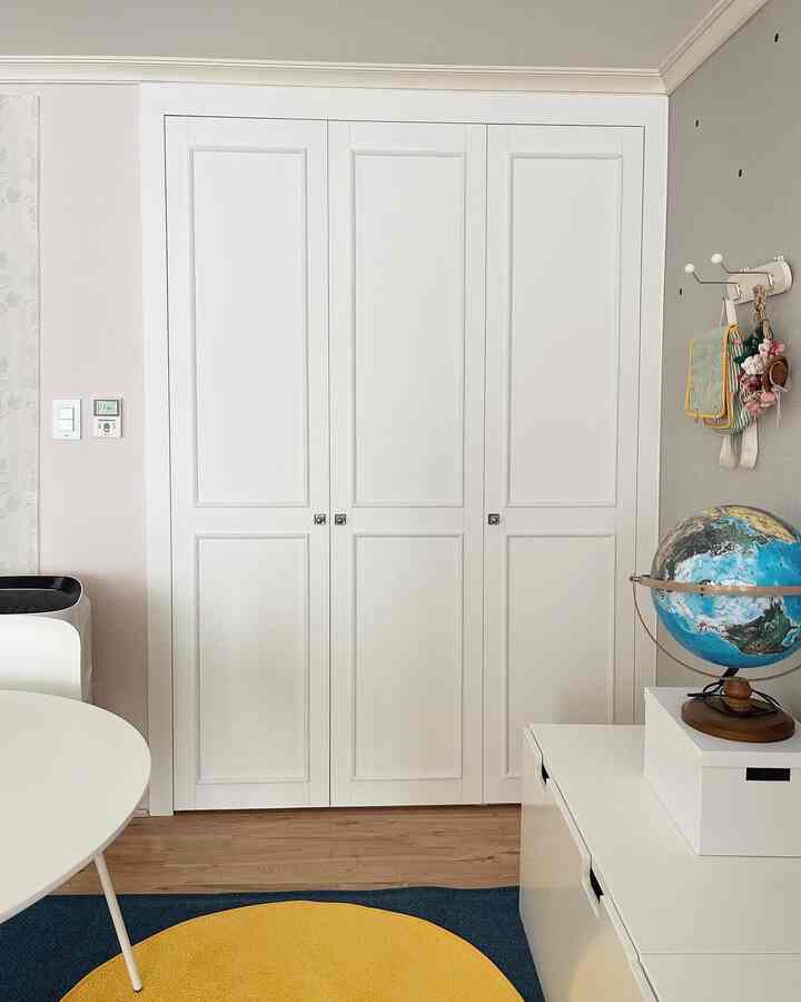 A clean and simple kids' room featuring a white built-in closet with wood tone flooring