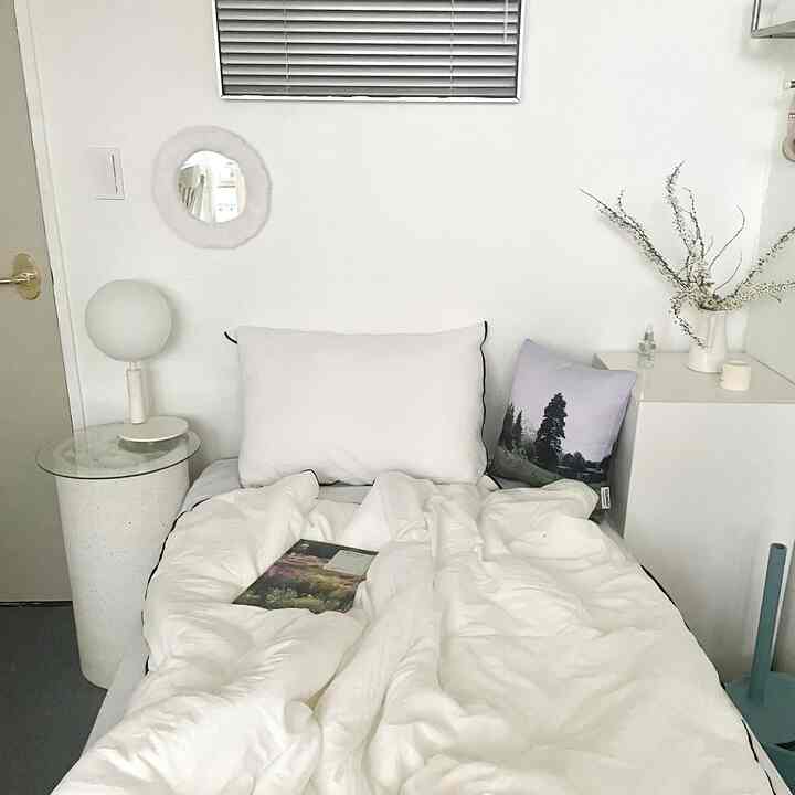 White-toned bedroom featuring a neat bed centered with nightstands, cushions, and a clean minimalistic atmosphere
