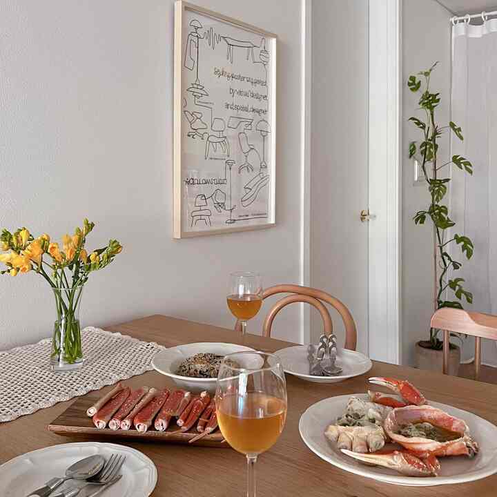 Beige and ivory toned dining room featuring wooden table and chairs, vase with flowers, and glassware in a natural setting