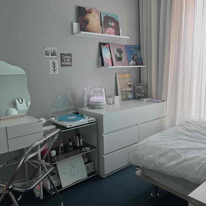 Monotone white and blue bedroom featuring minimalist furniture and shelves with posters, creating a neat home office and relaxation space