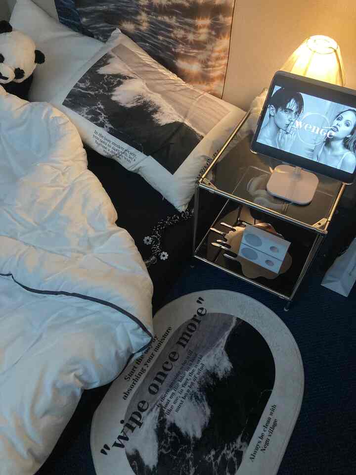 Monotone small bedroom featuring white bedspread, black rug, side table with iPad and lamp creating a cozy atmosphere