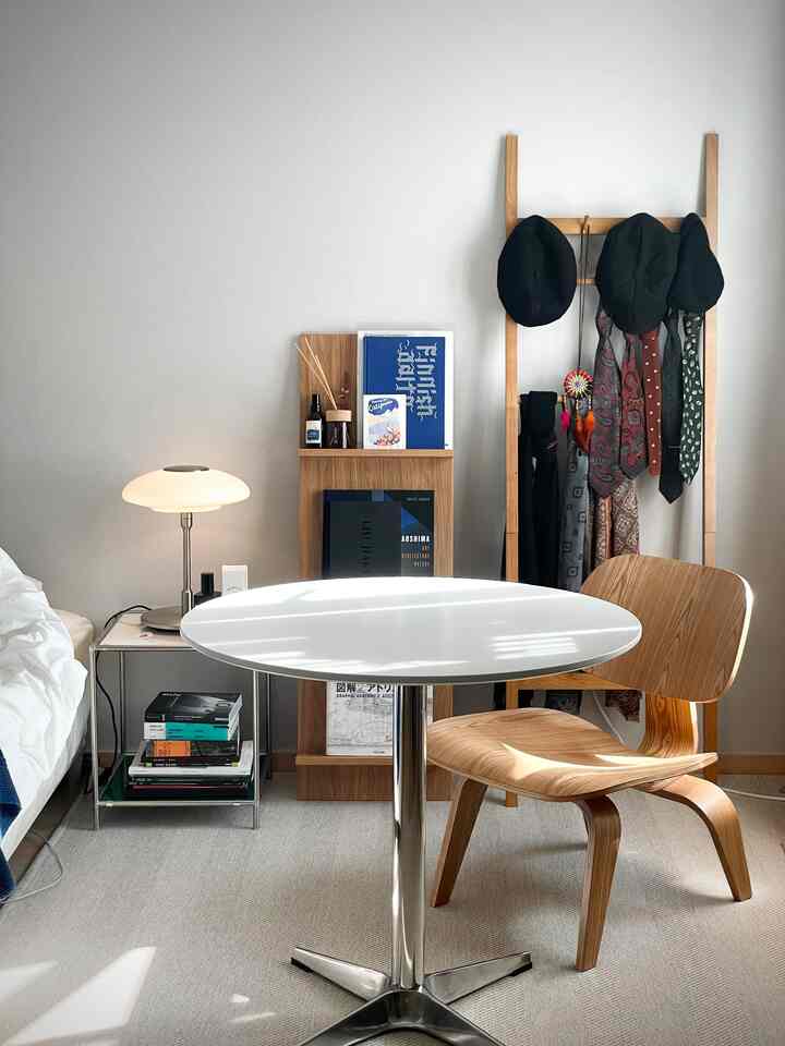 白と木目調が調和したコンパクトなワンルーム、実用的な家具と本棚、丸テーブルと椅子が配置された印象的な空間