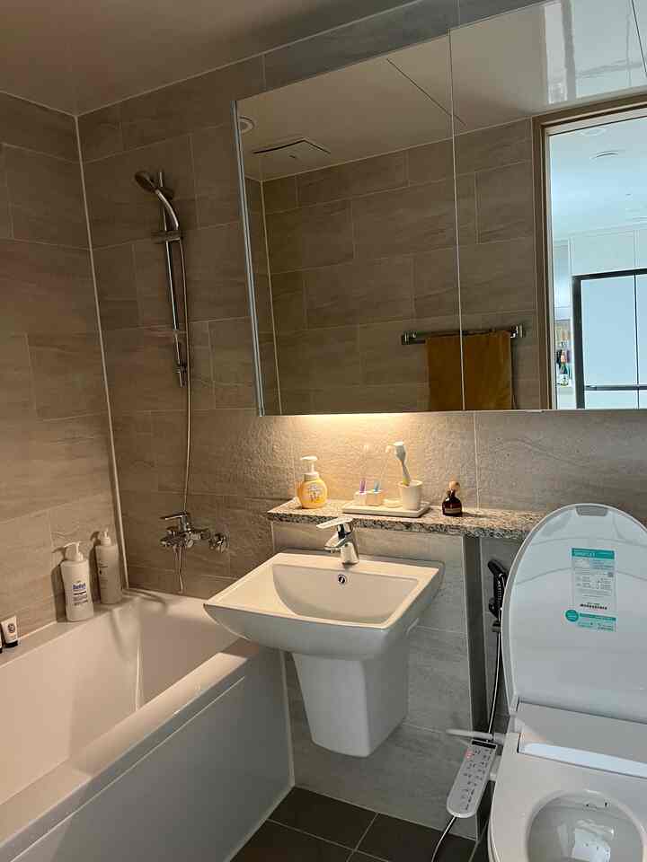 ベージュとホワイトのトーンのバスルーム、洗面台とトイレ、浴槽が整然と配置された空間