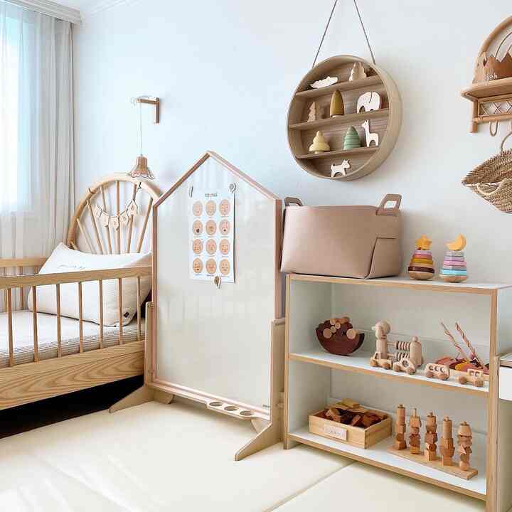 ベージュと木目調の調和が美しい赤ちゃん部屋、ベビーベッドとおもちゃ収納棚、丸い壁掛け棚が配置された清潔感のあるインテリア