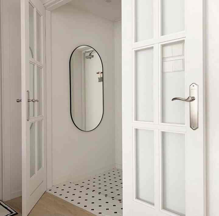Compact white and black monotone entrance featuring tiled floor and black-framed oval mirror in a simple space