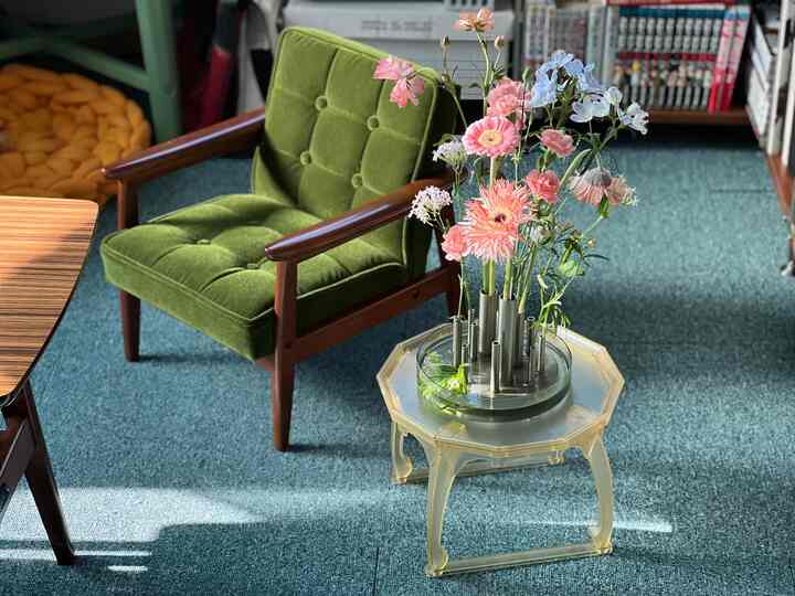 ティールカーペットの上にオリーブグリーンのアームチェアと花瓶が配置された雰囲気のあるリビング