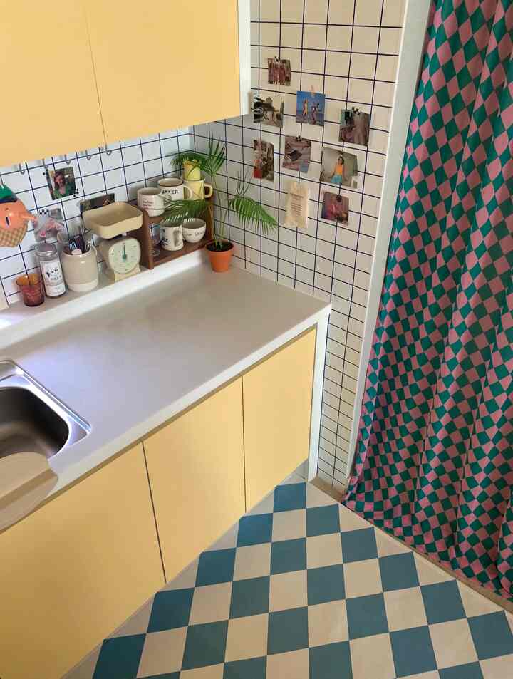 黄色と白色を基調としたキッチン、チェック柄のラグとピンク・グリーンのカーテンが配置された雰囲気のある空間