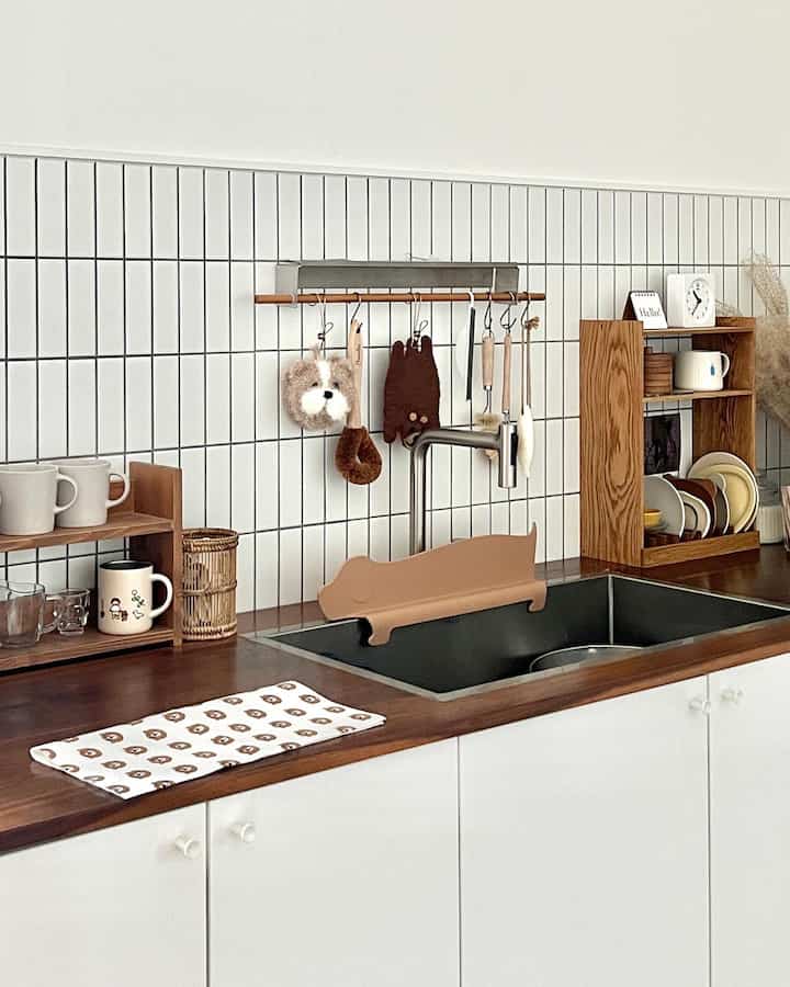 Clean kitchen sink area with bright white tiled walls and wood tone shelves arranged neatly