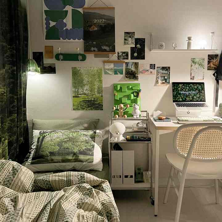 ホワイトとグリーンの色調の寝室兼ホームオフィス、壁に多くのポスターが飾られ、机にノートパソコンが置かれた落ち着いた雰囲気のインテリア