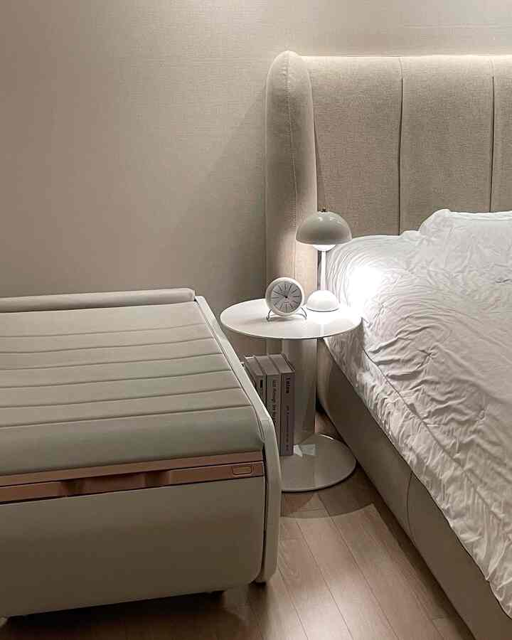 Beige-toned bedroom featuring a bed and a nightstand with a table lamp and clock, creating a clean and modern atmosphere