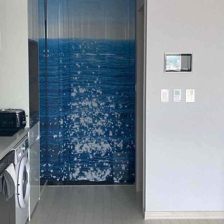 Gray monotone entrance area featuring a blue ocean print curtain and modern kitchen appliances with a clean atmosphere