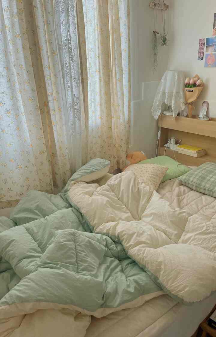 Pastel and ivory toned bedroom featuring floral curtains, lace lamp cover, and plush bedding with cushions creating a cozy atmosphere