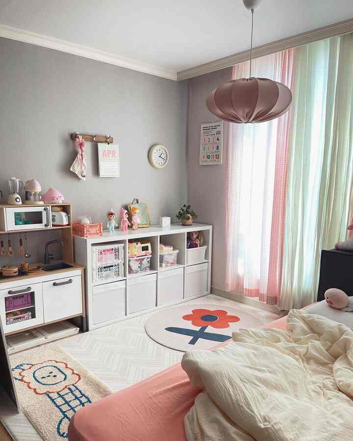 A cozy kids' room in gray and pink tones featuring toy storage shelves and a play kitchen set