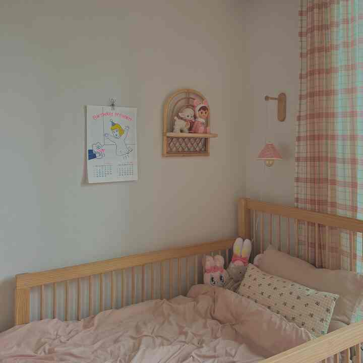 Beige-toned kids' room featuring a natural wooden bed with pink bedding, checkered curtains, and a baby poster on the wall, creating a cozy atmosphere