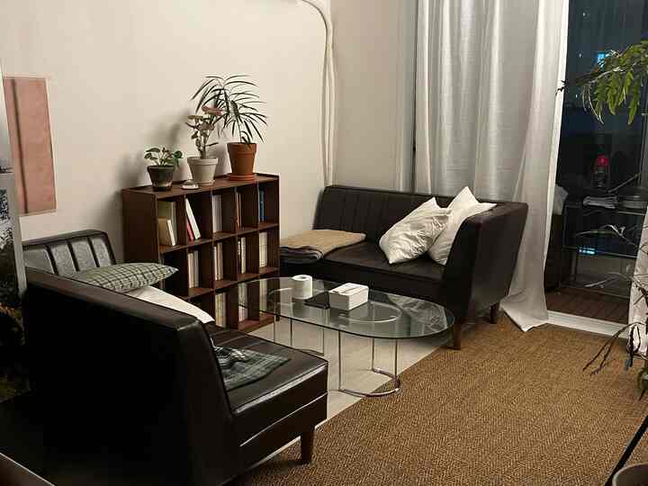 A natural-toned living room featuring two dark brown leather sofas, a clear glass coffee table, and a beige rug creating a cozy atmosphere