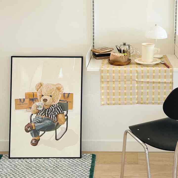White and beige toned small kitchen space featuring a poster frame and a mini dining table with lighting and cup, creating a cozy atmosphere