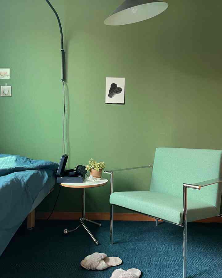 Green-tone bedroom featuring a mint armchair, white side table, and blue rug creating a cozy atmosphere