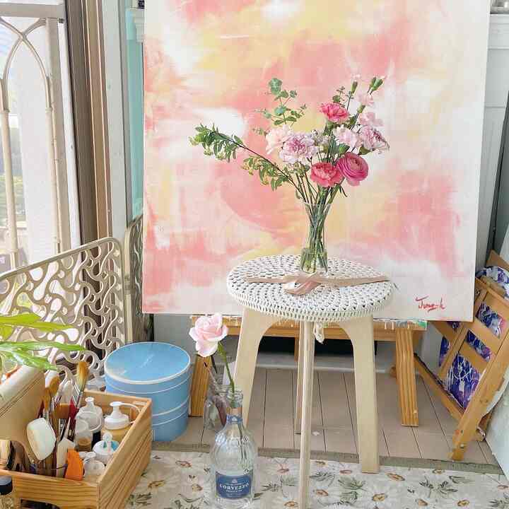 Pink and white toned art studio space featuring a stool with a vase and various art supplies, creating a cozy atmosphere