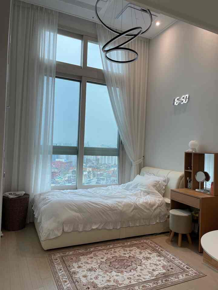 ホワイトとウッドトーンの調和が取れたワンルーム寝室、大きな窓とエレガントなラグが印象的な空間