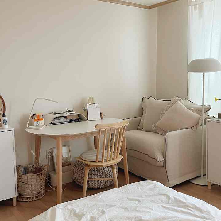A cozy studio apartment with white and beige tones, featuring a small desk and beige sofa harmoniously arranged