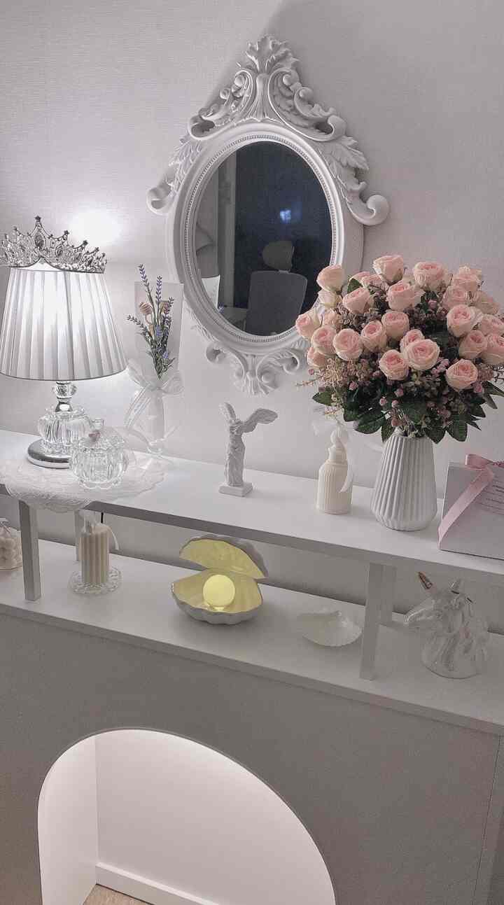 白を基調とした化粧台スペース、エレガントな鏡とピンクの花瓶、様々なオブジェや照明が配置された雰囲気のあるインテリア
