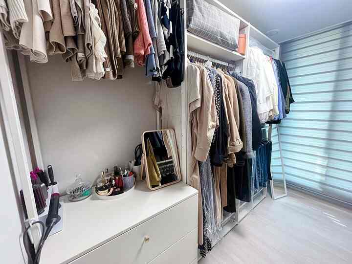 白とナチュラルカラーのウォークインクローゼット、システムクローゼットとドレッサーが配置された実用的な空間