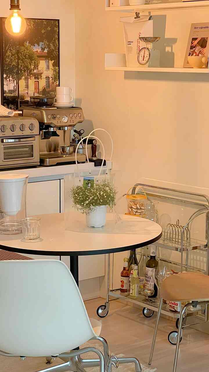 Warm beige-toned kitchen space featuring a round dining table, trolley, and coffee machine in a cozy home cafe setup