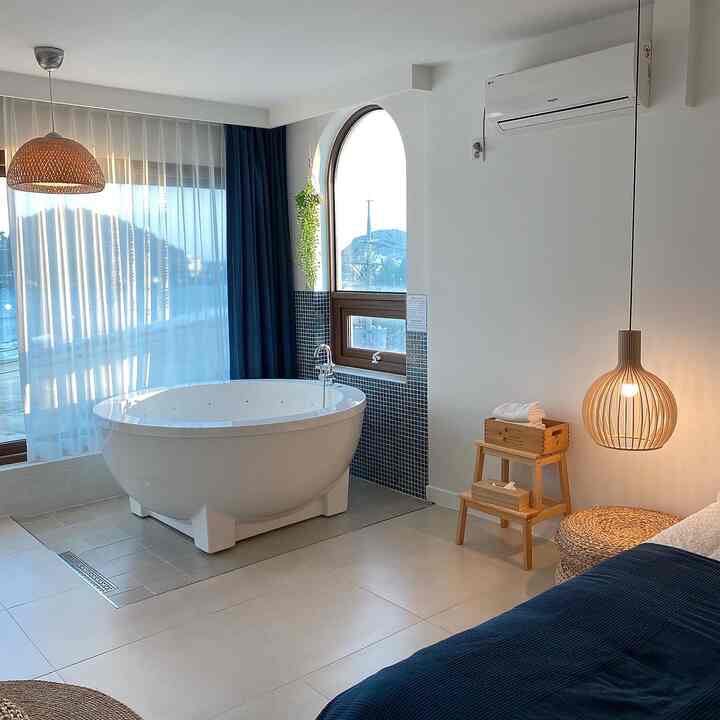 White-walled bedroom and bathroom space featuring a bathtub with wood-toned rattan lighting, creating a warm and natural atmosphere