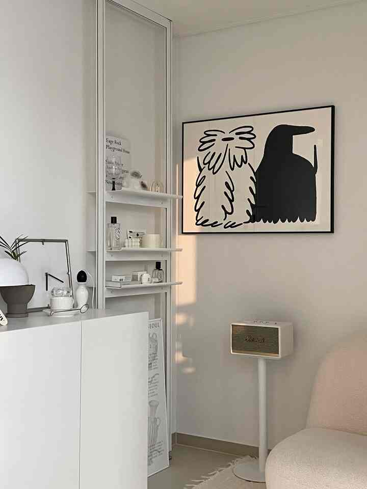 White-toned living room with minimalist modern furniture and objets, featuring illustrative framed artwork in a simple layout