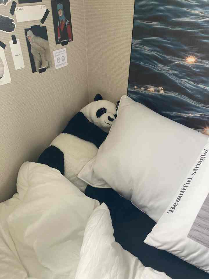 White and blue toned bedroom corner featuring a large panda plush and pillows in a cozy setting