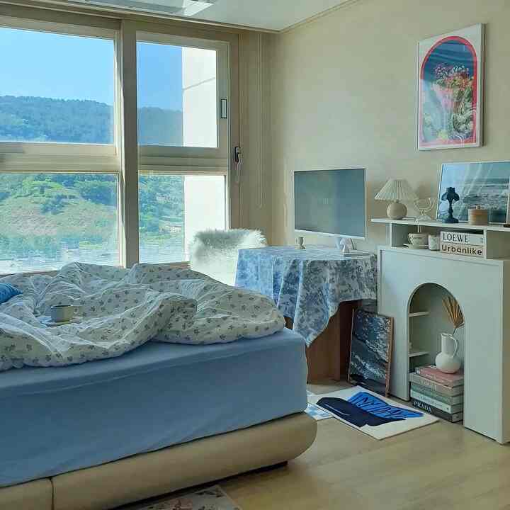 Blue and beige toned bedroom featuring a large window, bed with pillows and duvet, creating a cozy atmosphere