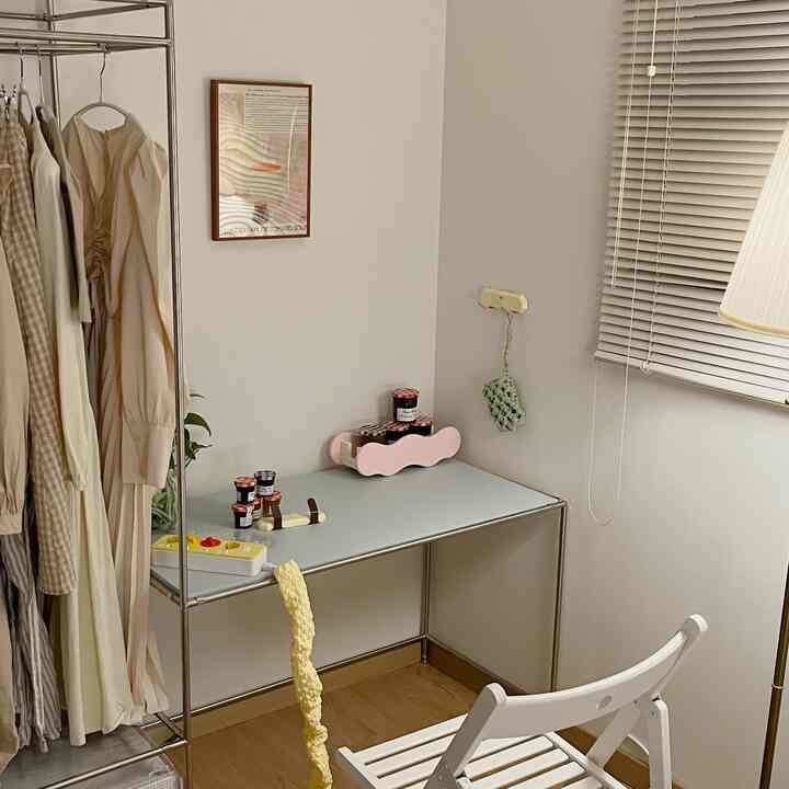 White and wood-tone small room featuring a coat rack, desk, and cat litter box with food bowls in a tidy home office setup