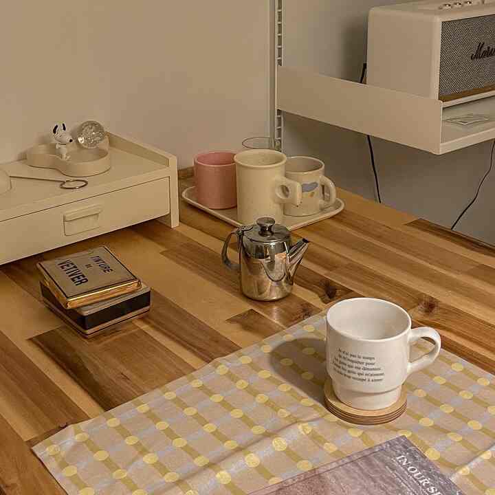Beige-toned wall and wood tone table featuring various cups and a tray in a cozy home cafe setting