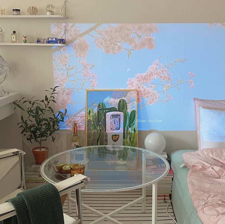 White and green toned studio bedroom with coffee table, plants, and cactus poster creating a natural and modern atmosphere