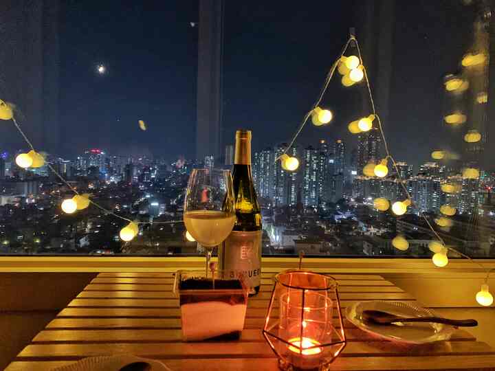 温かみのある木目調とストリングライトが配置されたベランダのホームバー、ワイングラスとキャンドルが雰囲気を演出