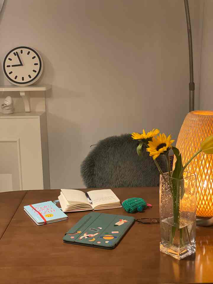 Natural color toned dining room featuring a large wooden dining table with a vase of flowers and notebooks, creating a cozy atmosphere