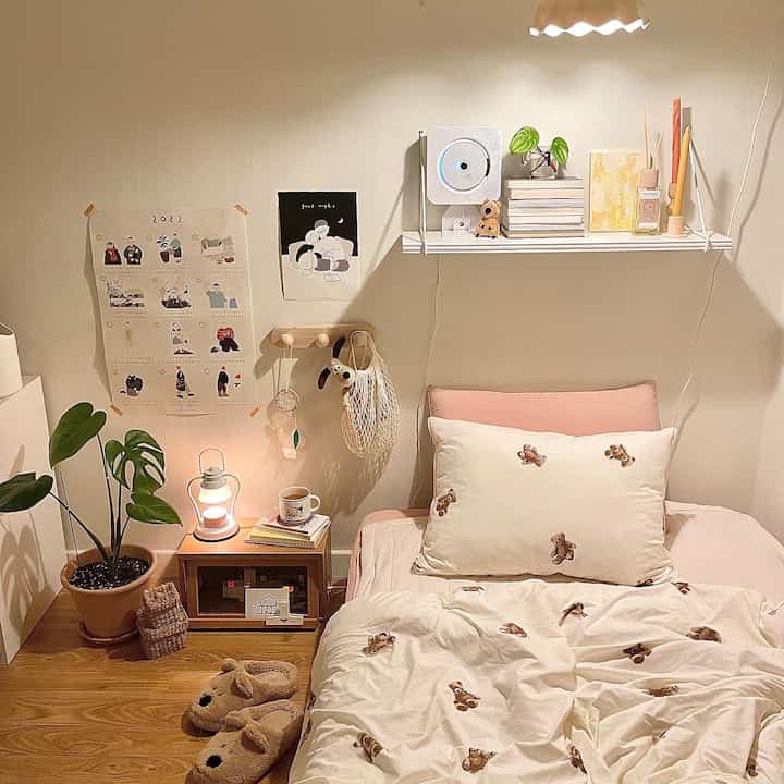 Natural-toned bedroom featuring pink bedding, wooden nightstand, diffuser and books on wall shelf, creating a cozy atmosphere