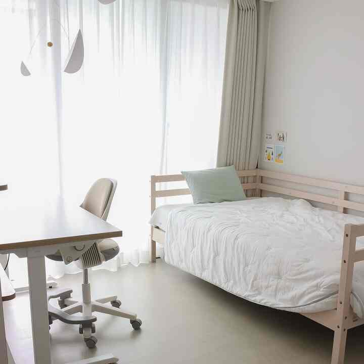 明るい白とナチュラルウッドの調和が取れた子供部屋、ベッドとデスク、チェアが配置されたシンプルで清潔感のある空間