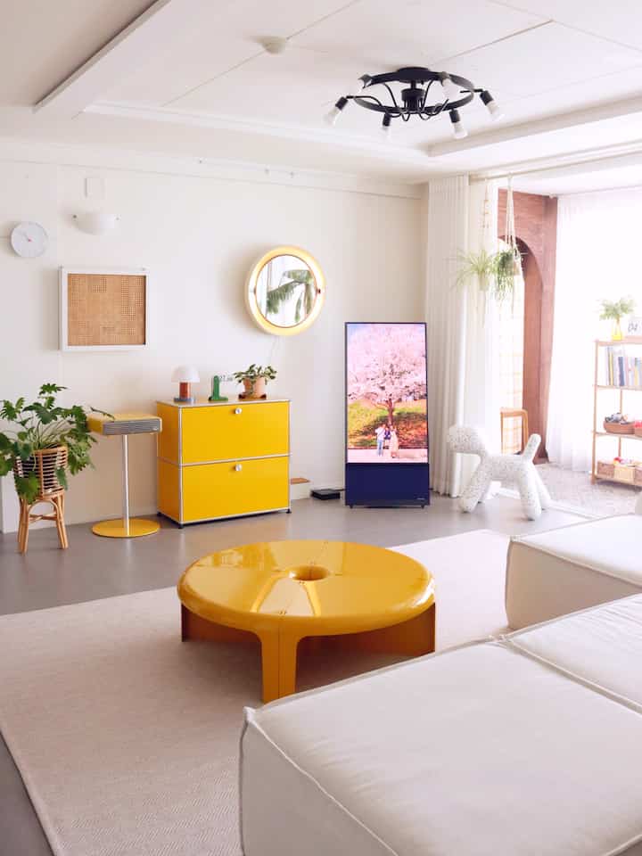 Bright white and yellow-toned living room featuring a yellow coffee table and sideboard, white sofa, and plants in a Nordic modern style