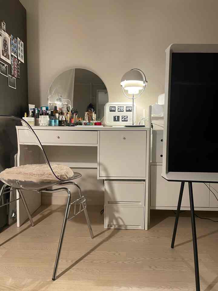 White-toned studio apartment vanity space featuring transparent stool and lighting with tidy interior setup