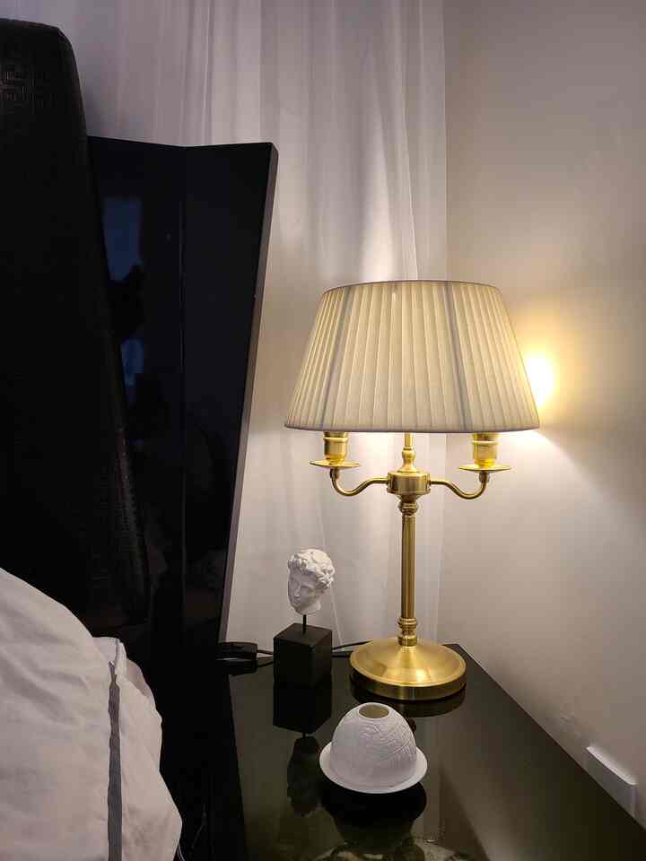Bedroom corner featuring a gold table lamp on a black bedside table with warm lighting ambiance