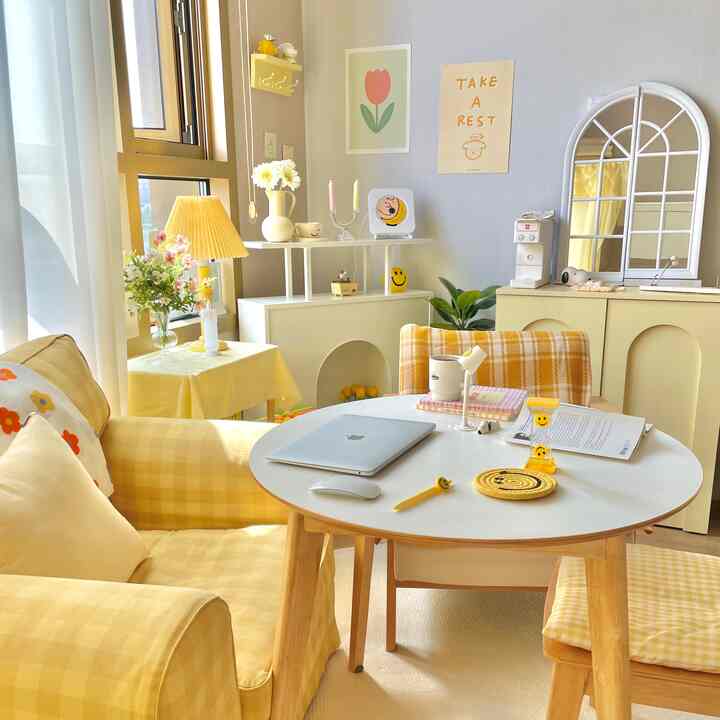 Yellow and cream-toned studio living room featuring a yellow checkered sofa, round table, and wall posters with cozy atmosphere