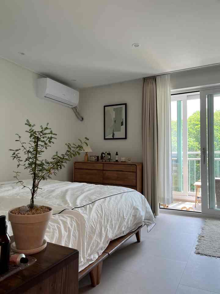 White and natural wood-tone bedroom with curtains and plant, creating a calm and natural atmosphere