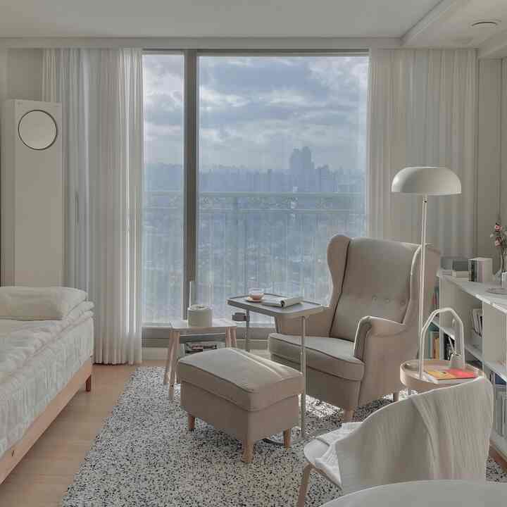 White and beige toned living room featuring armchair, stool, and curtains, creating a cozy reading nook