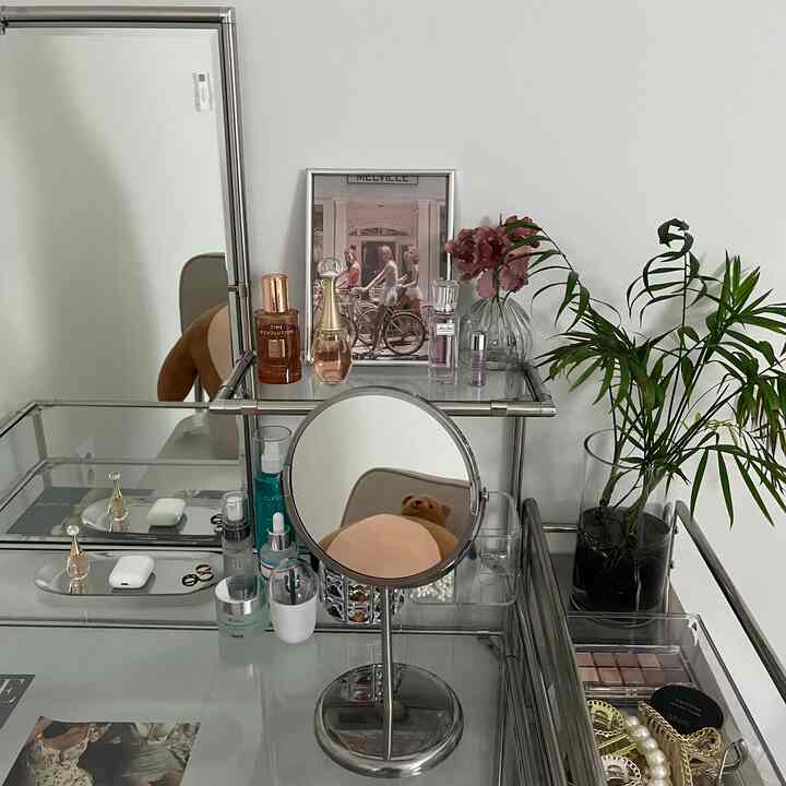 白い壁と金属製の化粧台およびテーブル、化粧台の横に置かれた緑の植物が調和するシンプルなインテリア空間