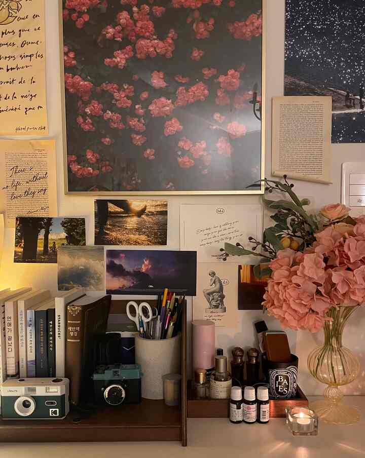 Brown wood-tone study area featuring pink flowers and a wall decorated with posters and postcards, creating a cozy atmosphere