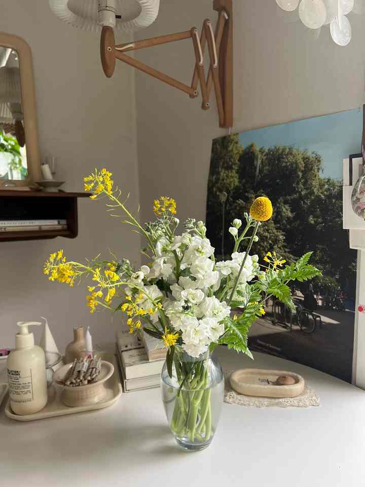 Natural and simple space with a transparent glass vase holding yellow and white flowers on a white-tone desk